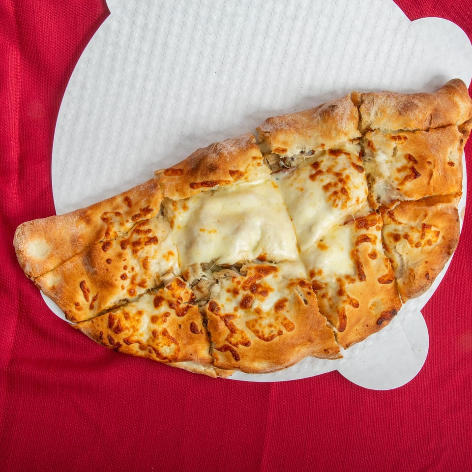 Sliced, golden-brown cheese-topped stuffed flatbread served on a white paper plate over red fabric.