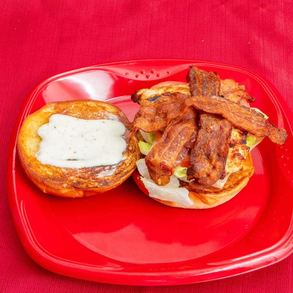 Bacon cheeseburger with lettuce and grilled chicken, served open-faced with creamy sauce on a red plate.