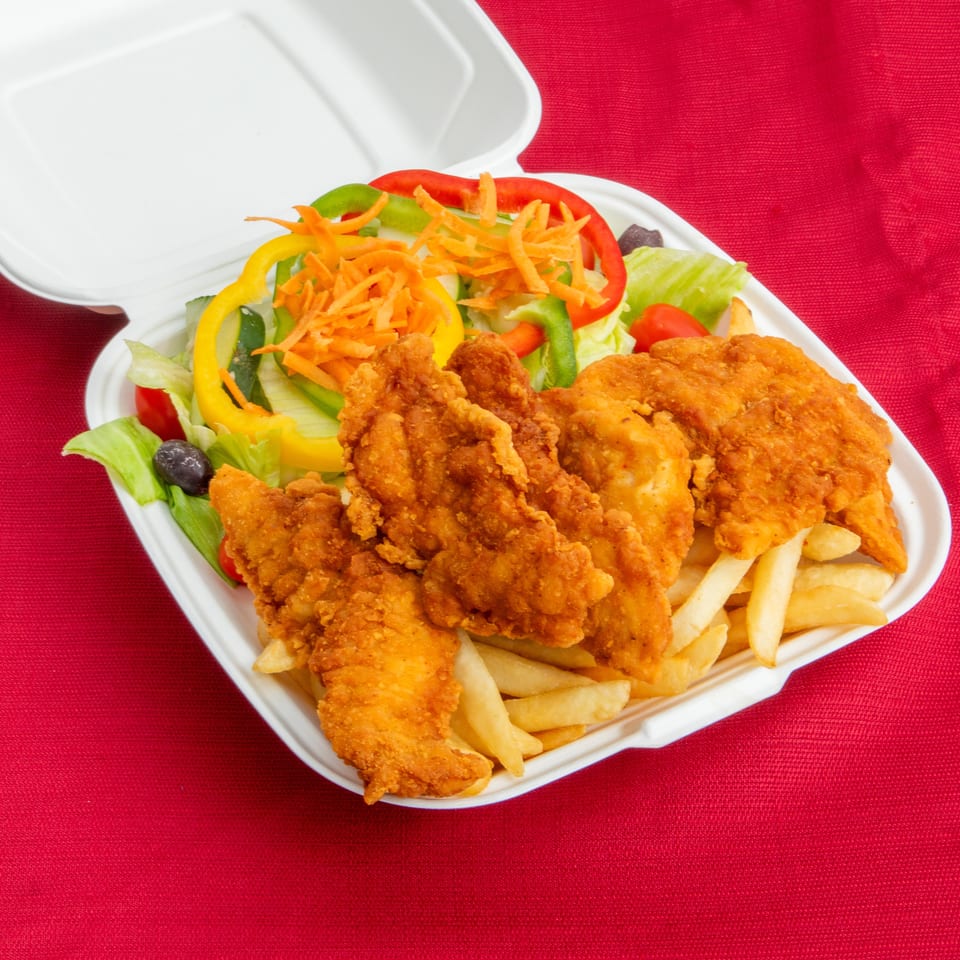 Crispy fried chicken pieces with French fries and a colorful salad served in a white takeout container on red fabric.